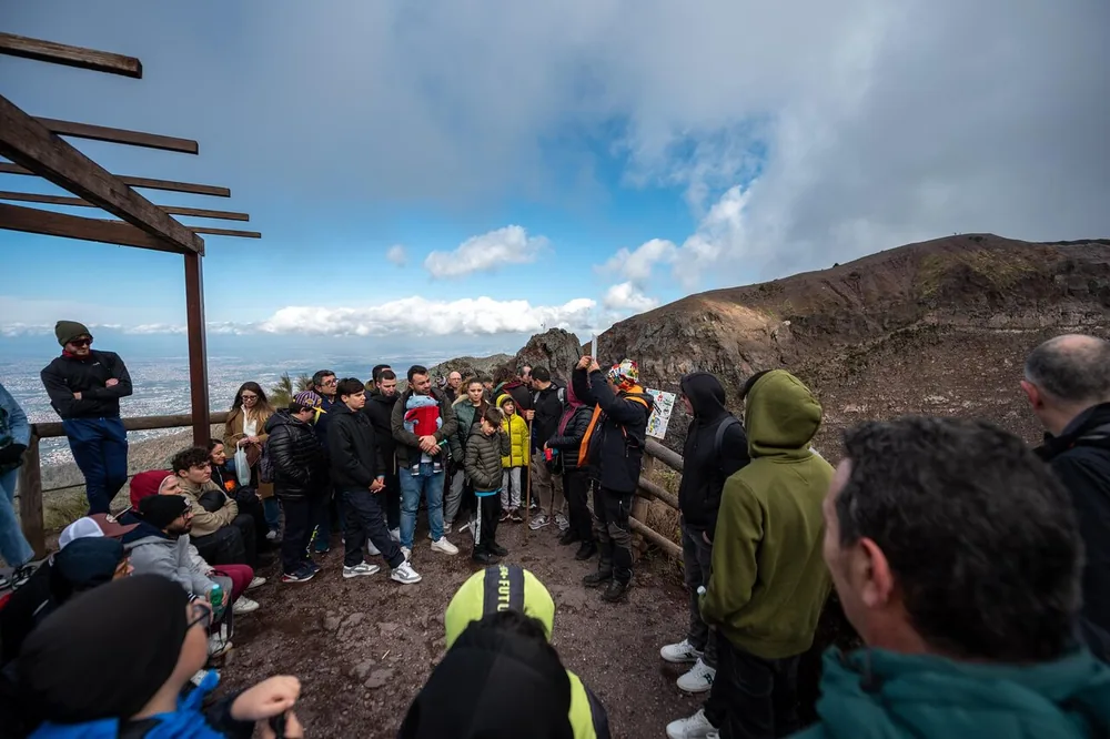Visitors in jackets and hoods gathered at the crater rim of Vesuvius under a cloudy sky